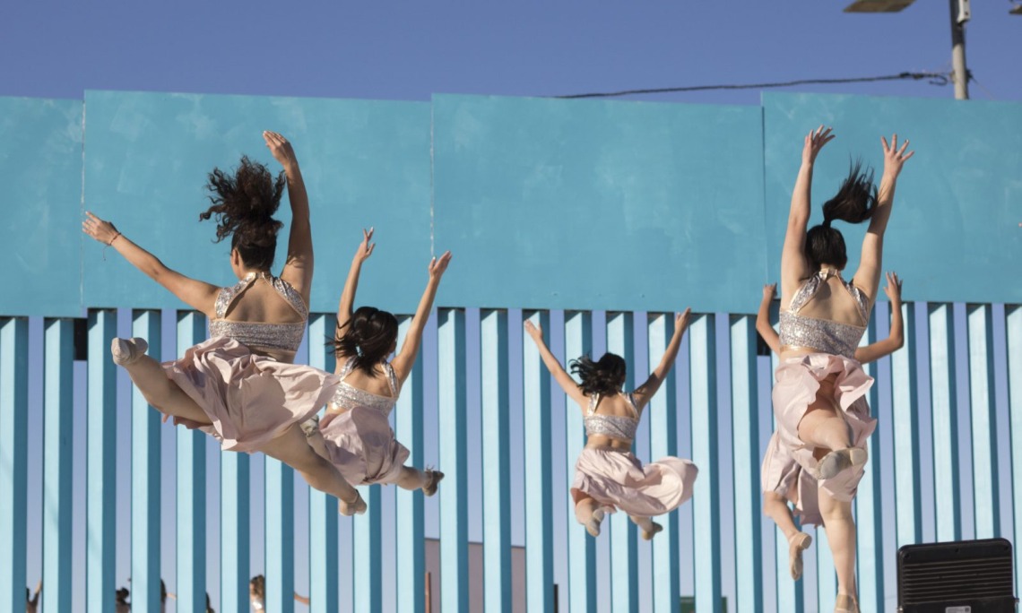 Ballet dancers leaping in front of the border wall